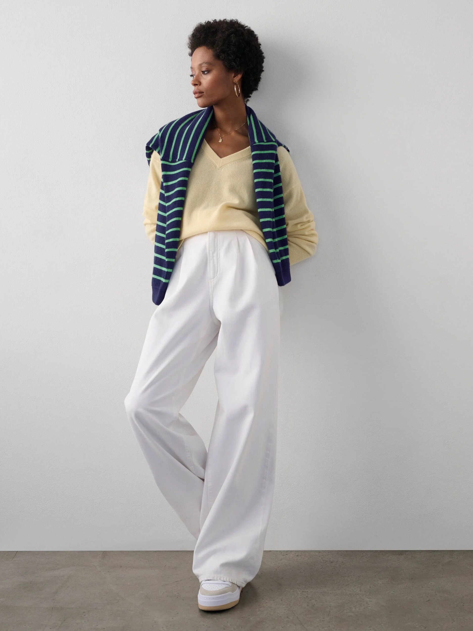 A model wearing a yellow v-neck cashmere sweater with a blue and green striped sweater thrown over their shoulders, from White & Warren.