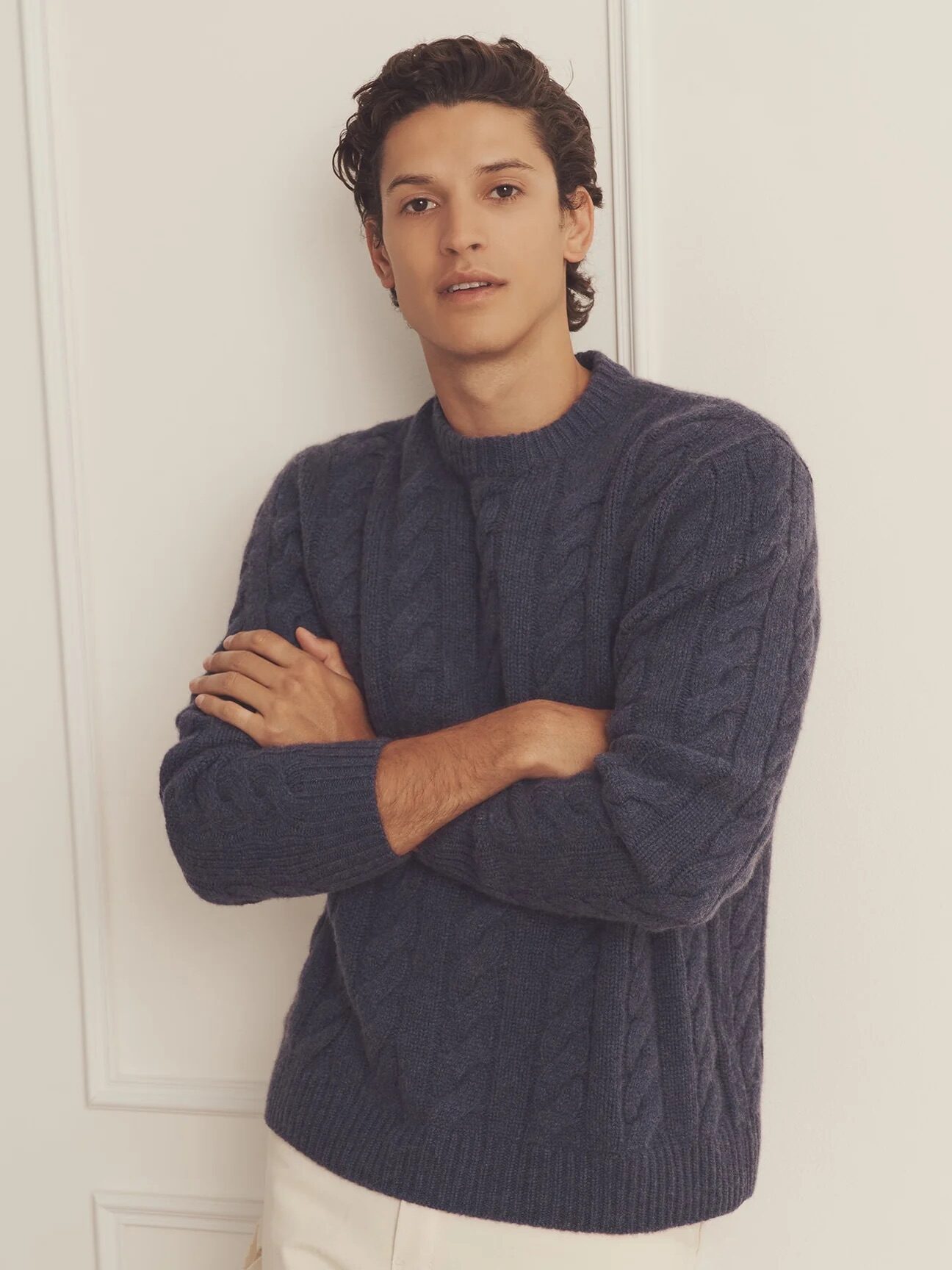 A model wearing a NAADAM cable-knit sweater in a dark blue color.