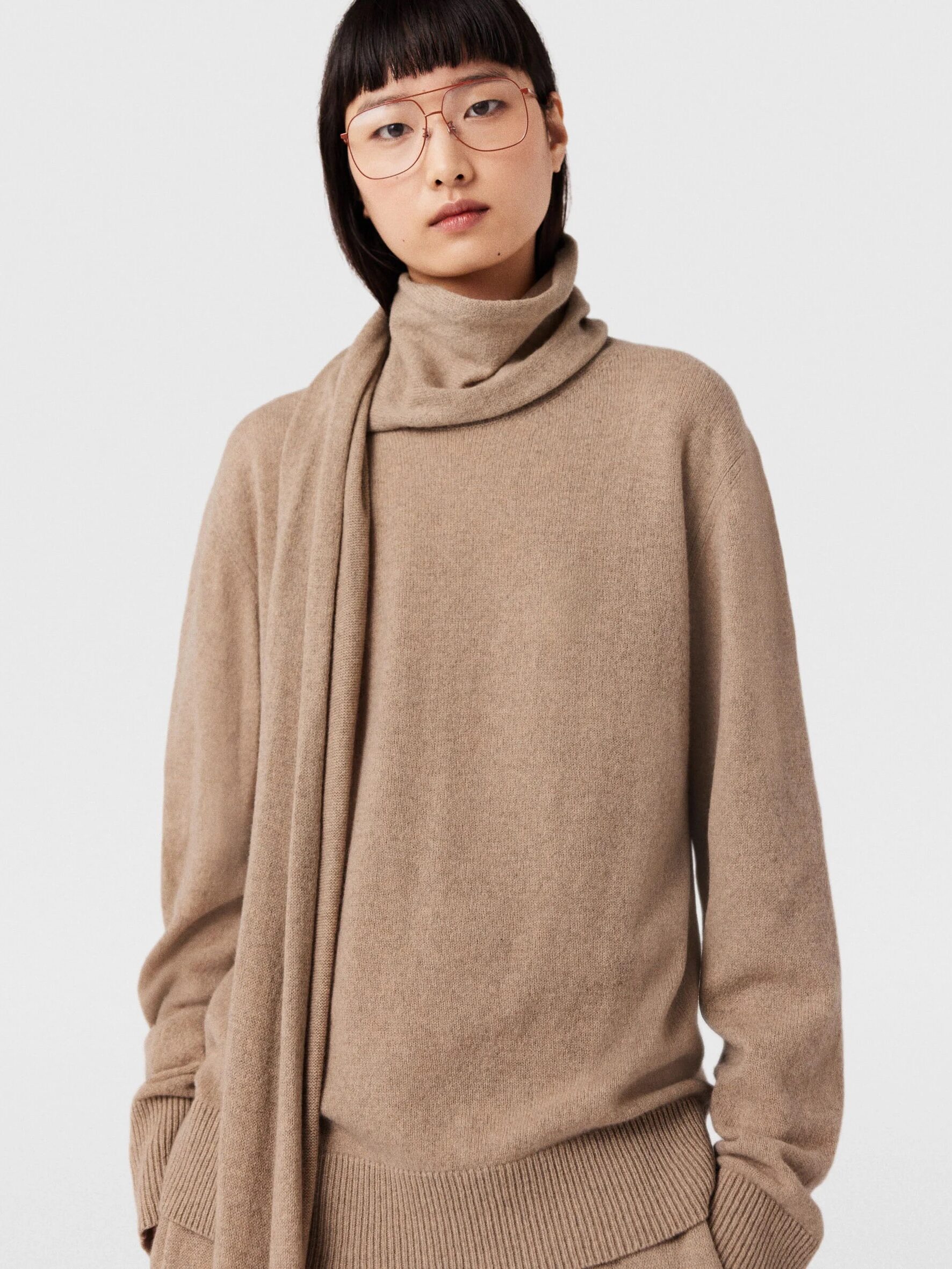 A model wearing a beige cashmere turtleneck with an attached scarf from Stella McCartney.