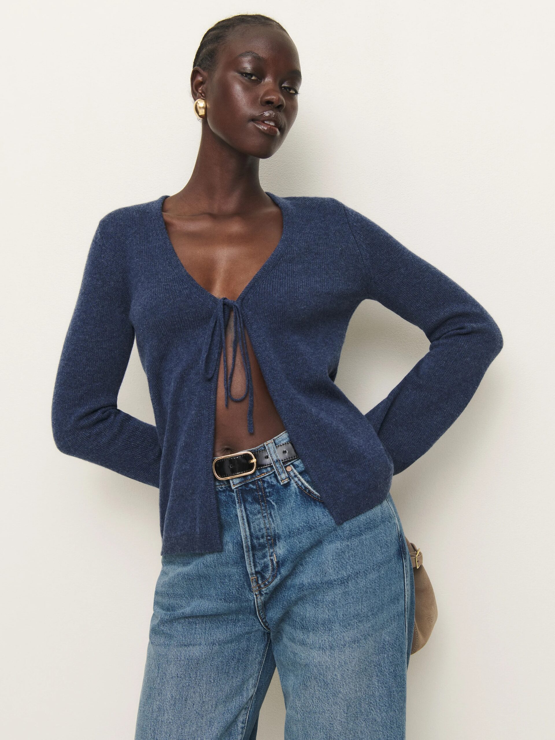 A model wearing a dark blue cashmere tie-front cardigan from Reformation.