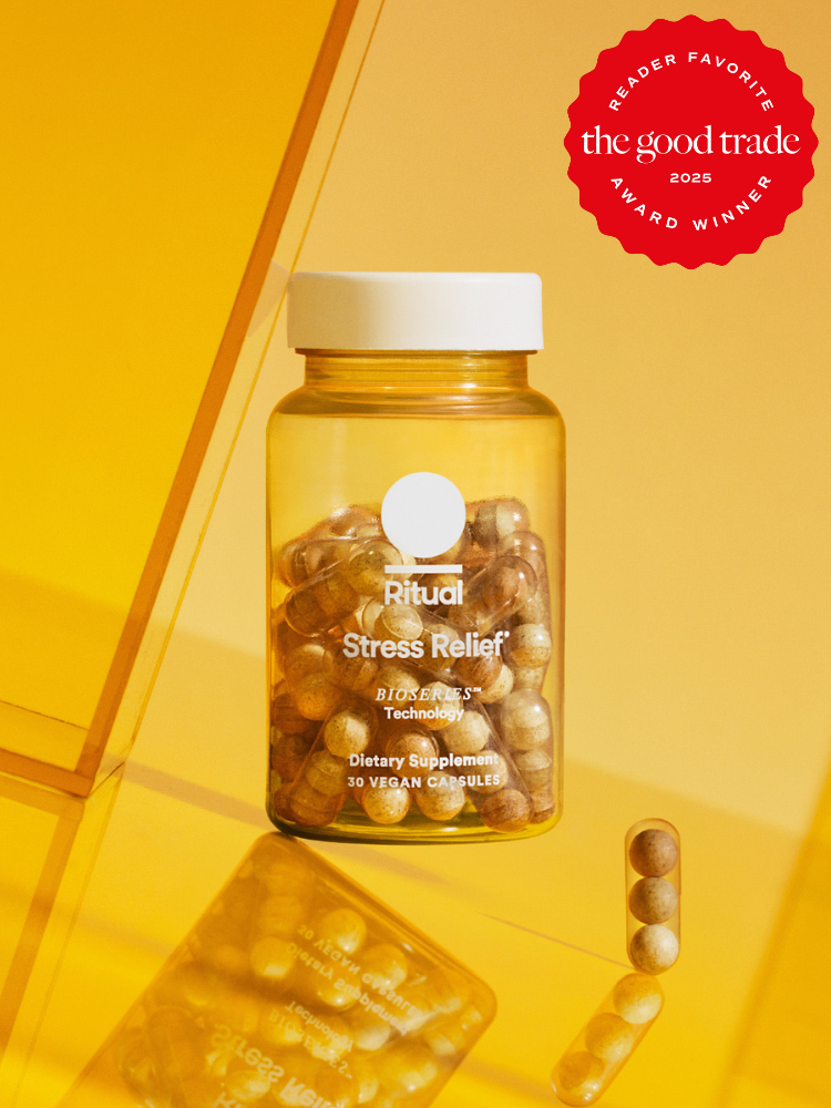 A bottle of Ritual Stress Relief vegan capsules sits on a reflective yellow surface. A "Reader Favorite" award badge from The Good Trade, 2023, is displayed in the upper right corner.